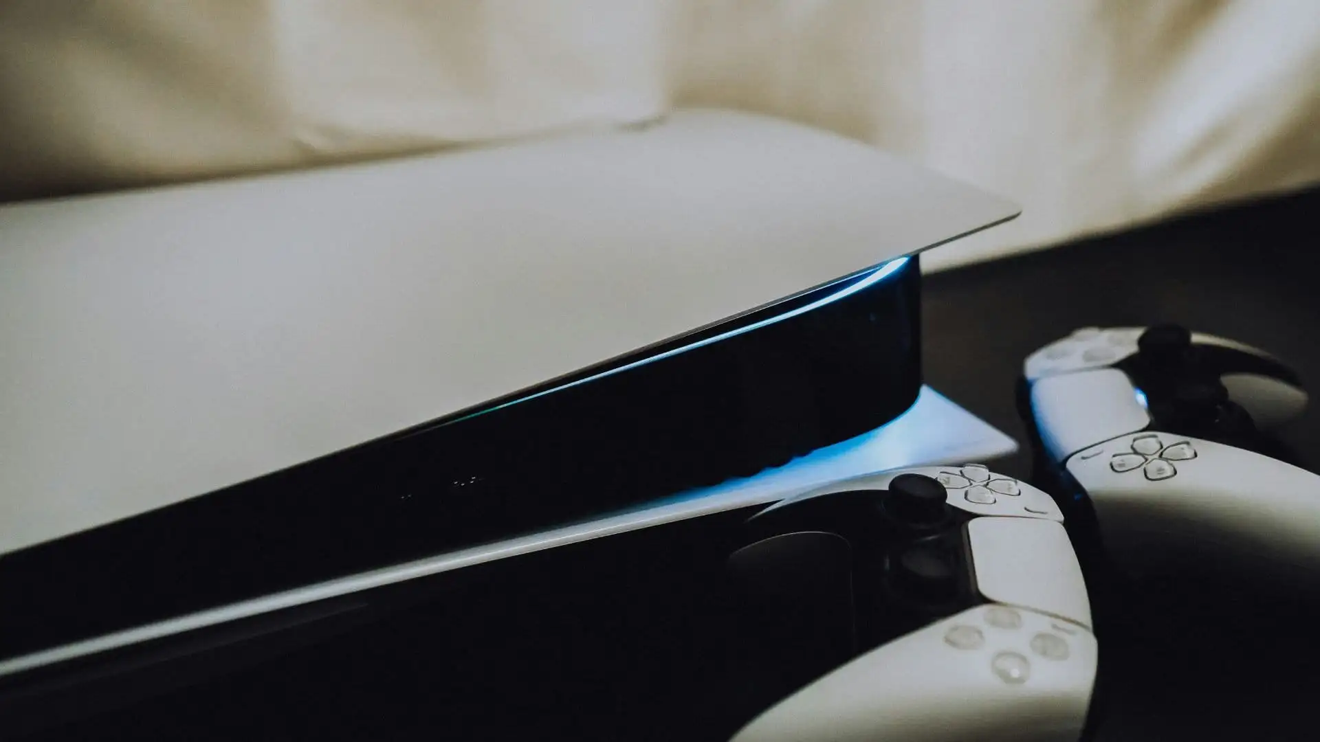 Close-up of a PlayStation 5 console with two DualSense controllers on a dark surface
