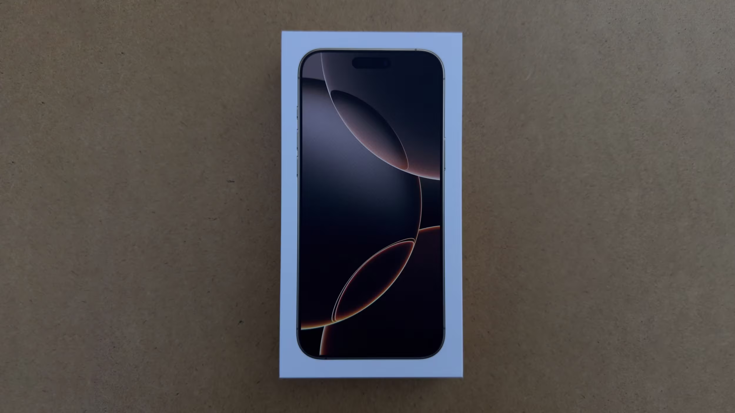 Front of iPhone 16 shown inside its box against a brown surface