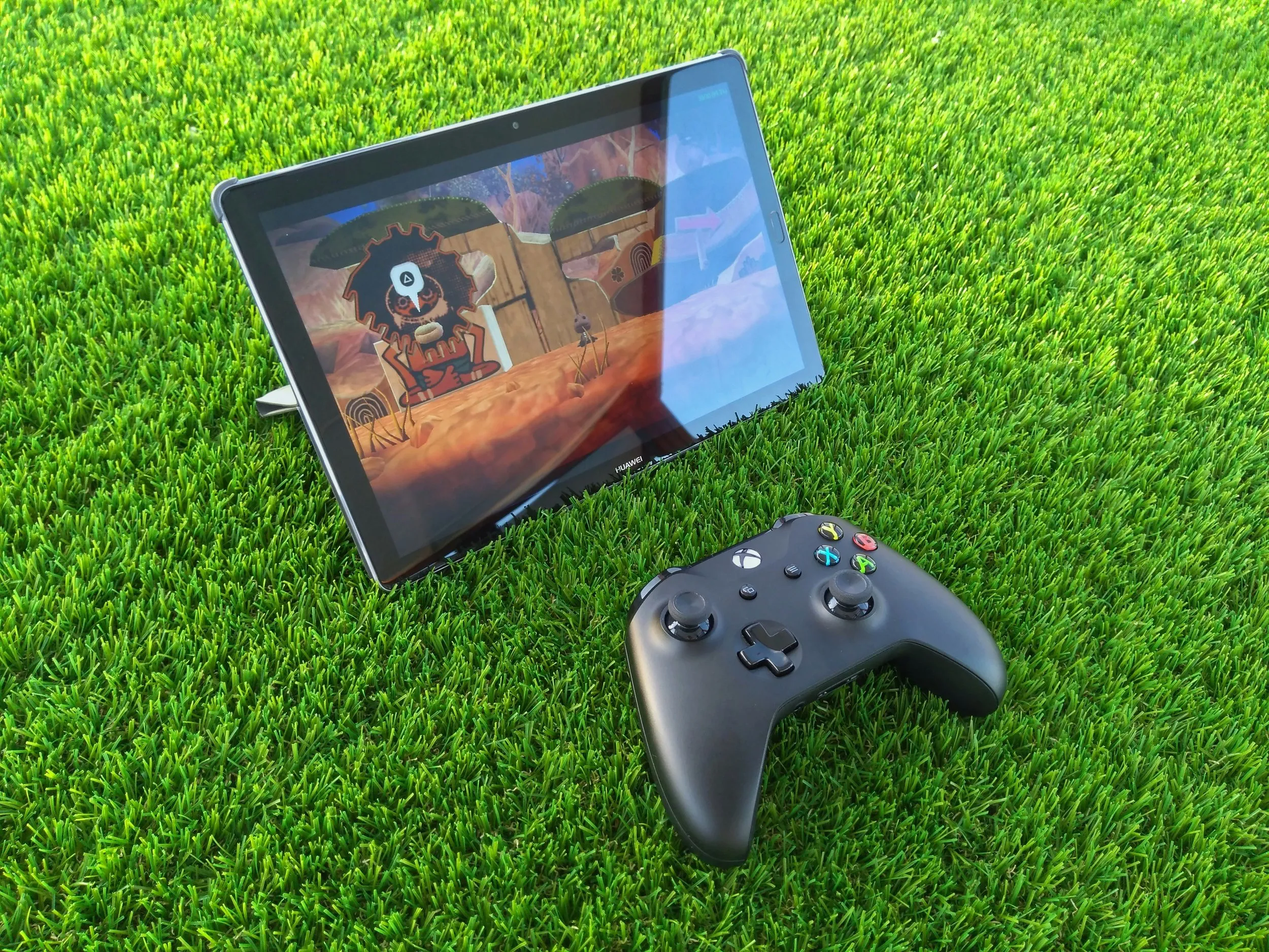 Xbox controller and tablet running a game on green grass, showing outdoor cloud gaming setup.