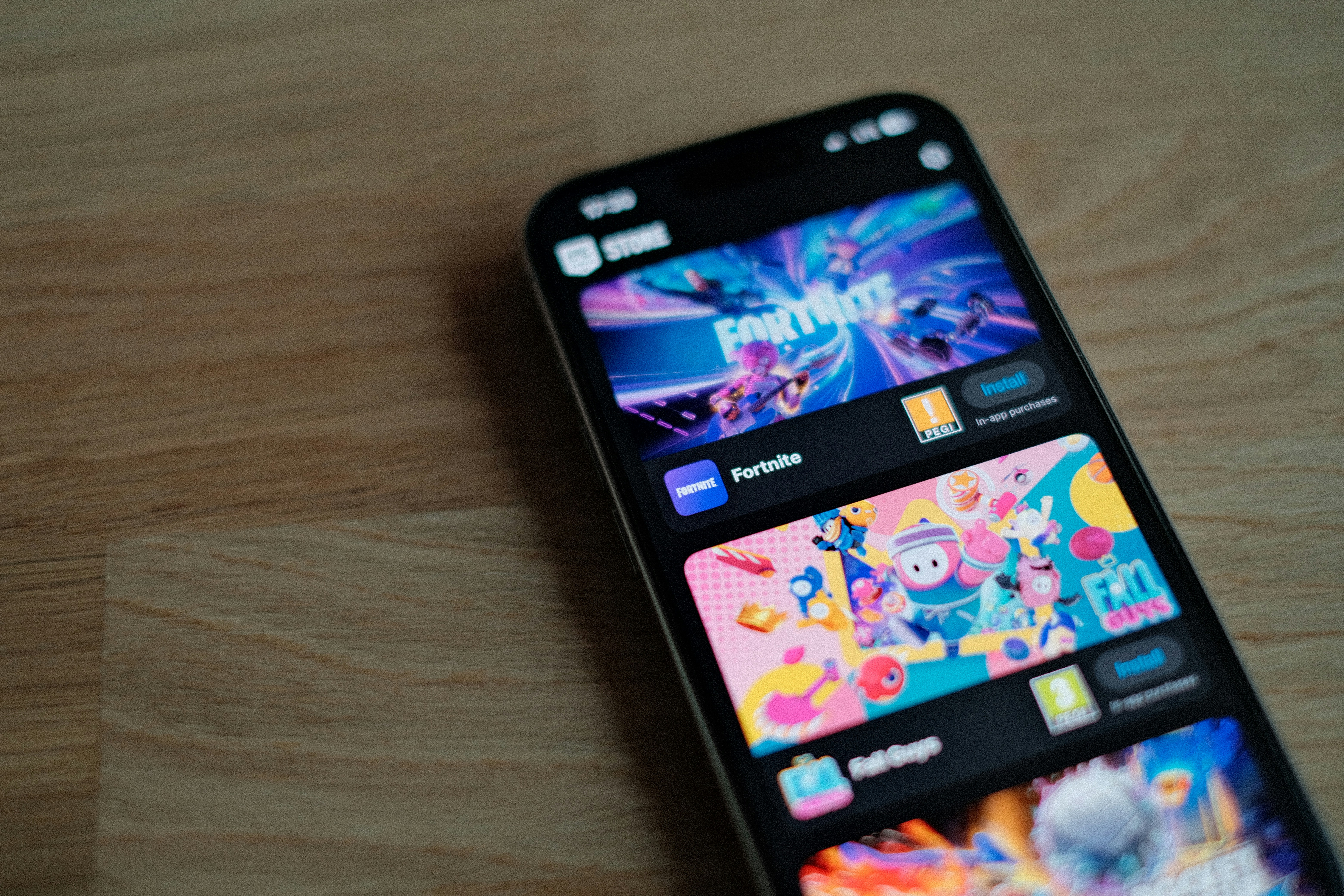 A smartphone displays the Epic Games Store app with download options for Fortnite and Fall Guys.