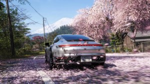 A silver Porsche drives down a road covered in pink cherry blossom petals with Mount Fuji in the background.