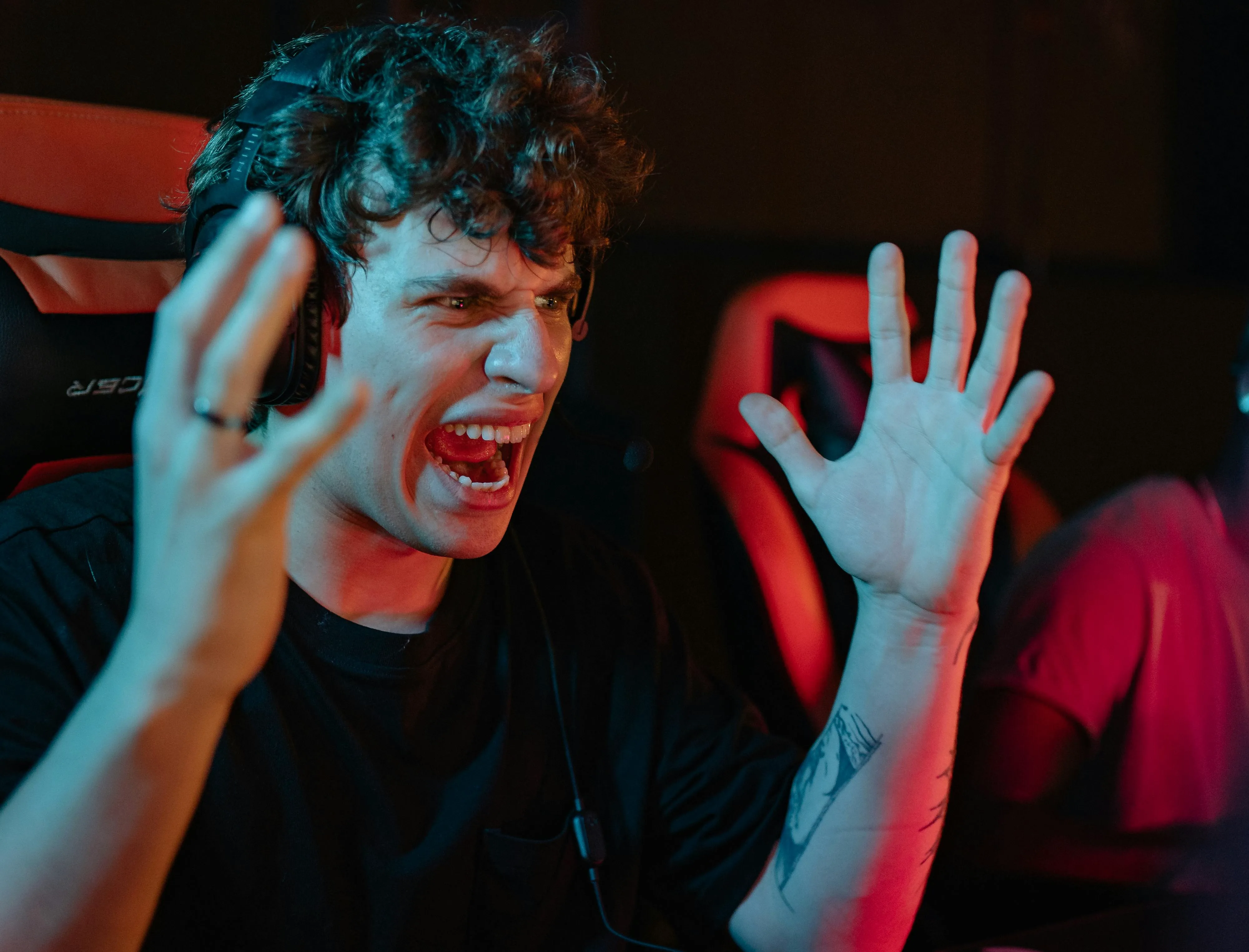 A frustrated gamer wearing a headset shouts and throws his hands up during a competitive match.