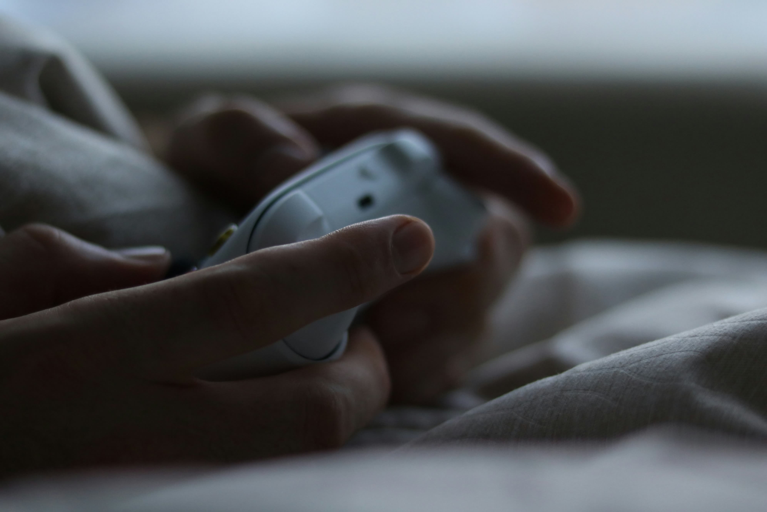 Close-up of hands holding a game controller while resting on a bed.