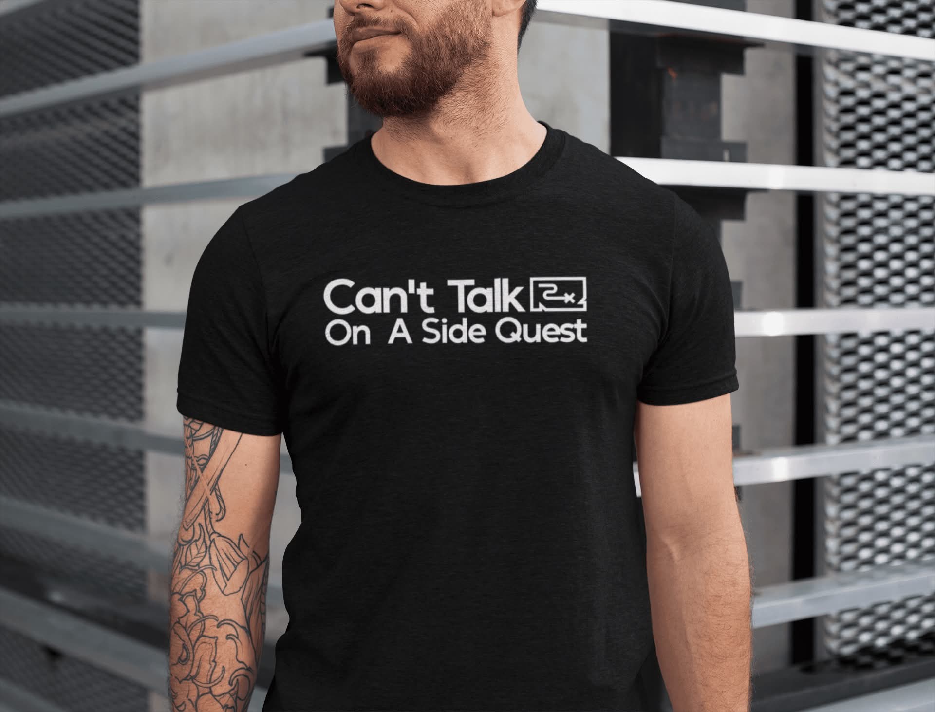 Mockup of a man with tattoos wearing a black t-shirt with the text "Can't Talk On A Side Quest".