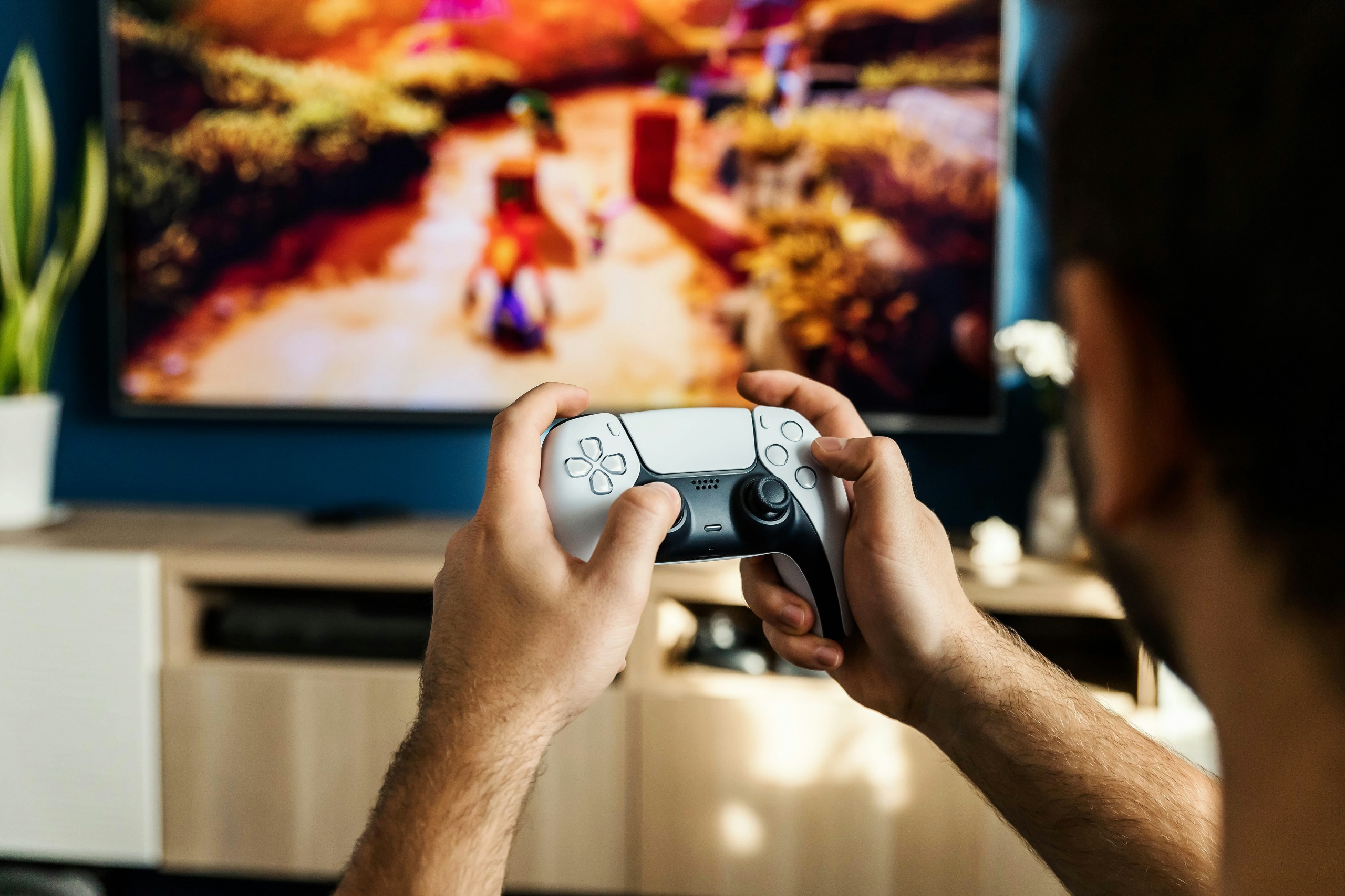 Individual holding a PlayStation 5 controller while watching a game on a television screen.