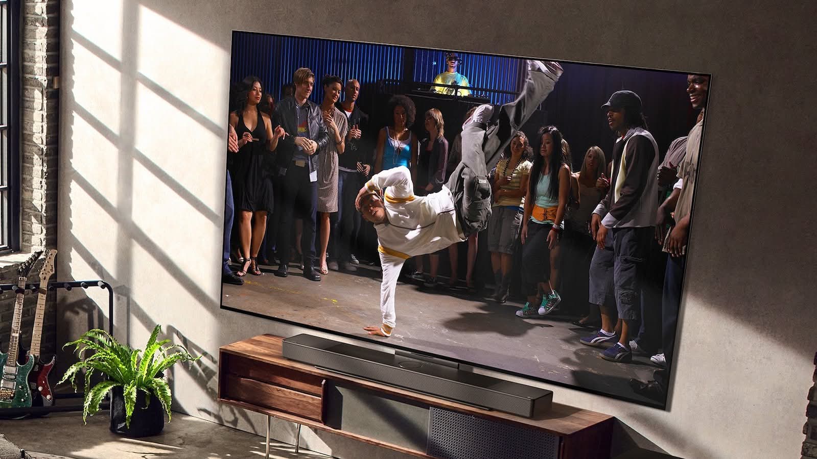 large LG OLED C3 Series 4K TV displaying a video, with a soundbar below it and guitars and a plant to the side