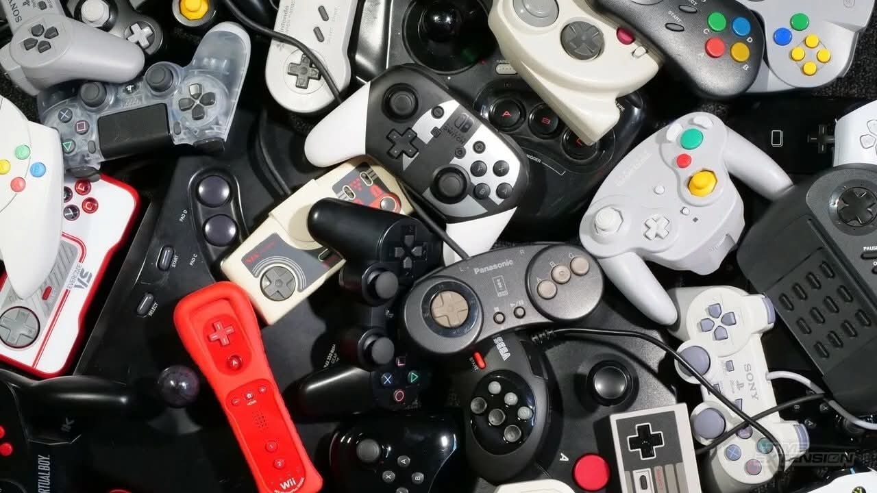 Top-down view of a large pile of assorted game controllers from different gaming systems and eras.